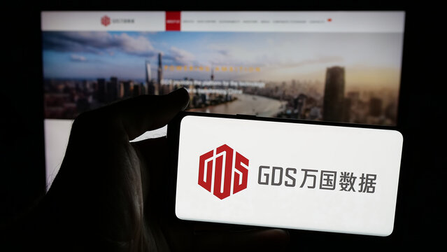 Stuttgart, Germany - 06-06-2025: Person holding mobile phone with logo of Chinese data center company GDS Holdings Ltd. on screen in front of web page. Focus on phone display.