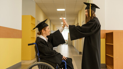 Happy young woman and woman in wheelchair in graduate gown with diploma in hands. Inclusive...