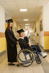 Happy young woman and woman in wheelchair in graduate gown with diploma in hands. Inclusive...