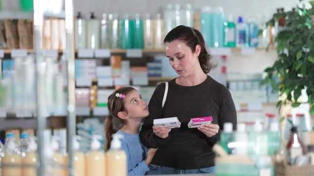 Adult woman with daughter buyers choosing box of paracetamol tablets in pharmacy