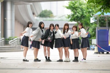 Fototapeta premium In early summer in Shanghai, near The Bund, Japanese high school girls in uniforms stand on a city street, posing for a commemorative photo, their smiles adding charm to the vibrant urban scene.