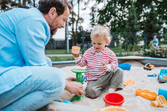 Father and little toddler son playing in the sandbox on playground.