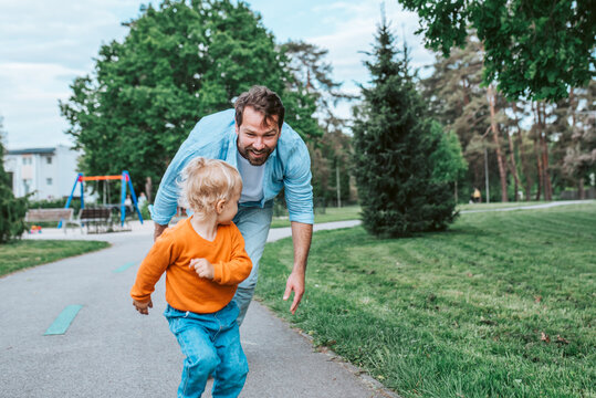 Father running with toddler son, chasing him for fun in park