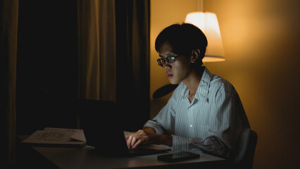 Overworked Asian Man Working Late at Night on Laptop at Home.