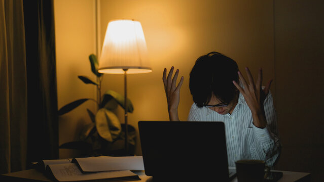 Asian freelance worker experiences frustration and emotional fatigue while working overtime late at night in a home office