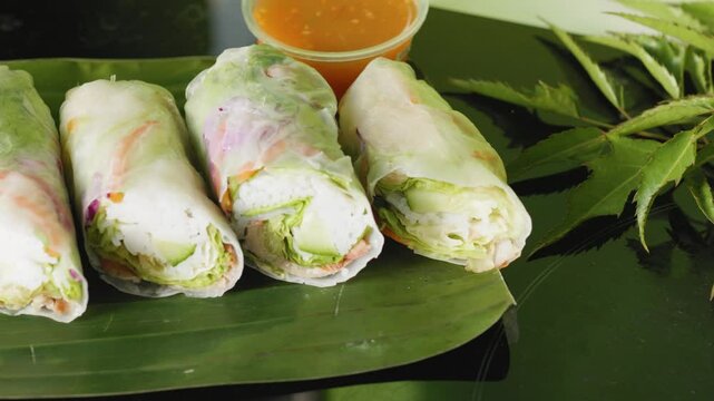 Vietnamese summer rolls displaying crisp vegetables, succulent shrimp, and fragrant herbs nestled on banana leaf with zesty dipping sauce, highlighting fresh culinary artistry