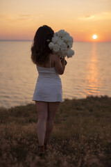 Happy woman holding a bouquet of flowers at sunset on a top above the sea