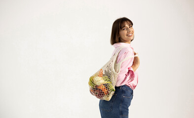 Smiling woman on white cyclorama holding broccoli and flexing biceps. Promoting healthy lifestyle,...