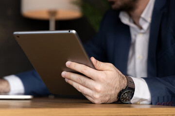 Businessman in suit sitting on orange sofa in office, talking on phone and using tablet and laptop....