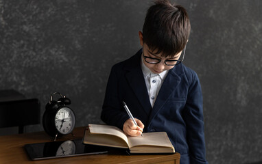 School-age boy sleeping at desk with crooked glasses and small alarm clock nearby. Child smiling...