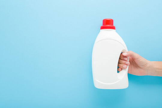 Young adult woman hand holding white plastic container on light blue wall background. Pastel color. Cleaning detergent, washing liquid or body care product. Closeup. Empty place for text. Front view. - Powered by Adobe