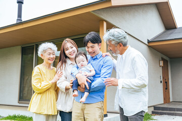 住宅の前で笑顔で赤ちゃんを囲む三世代家族