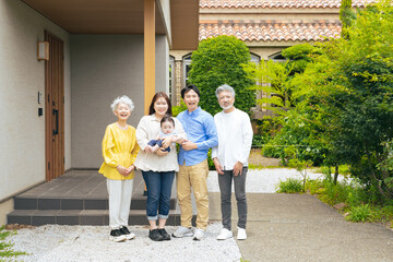 住宅の前で笑顔で赤ちゃんを囲む三世代家族