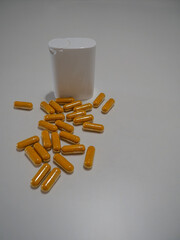A group of capsules spilled next to a white plastic container on a plain background, highlighting...