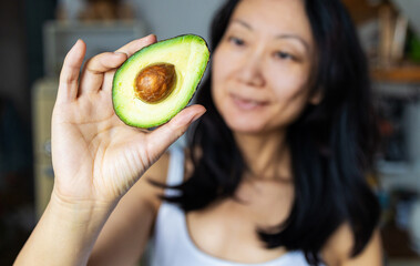 Asian woman holding half an avocado in her hand, healthy eating and raw food concept