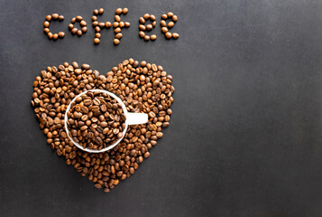 From above close-up view of roasted coffee beans in a white cup on a textured black surface,...