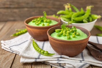 Green pea soup on a wooden table. Fresh pea soup bowl. Delicious healthy cream soup in a bowl with green peas and croutons. Healthy vegan puree. Copy space. Space for text.