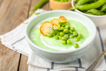 Green pea soup on a wooden table. Fresh pea soup bowl. Delicious healthy cream soup in a bowl with green peas and croutons. Healthy vegan puree. Copy space. Space for text.