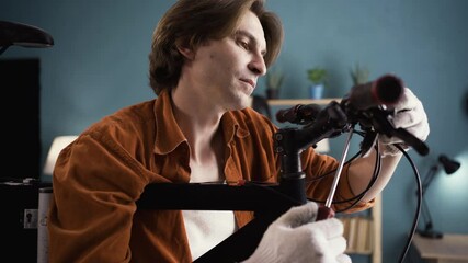 Young man repairing bicycle on a repair stand fixing handlebar with screwdriver in home workspace.