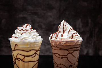 Vanilla and chocolate milkshakes with chocolate syrup in clear glass on dark background