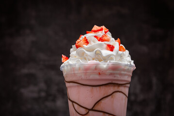 Strawberry milkshake with chocolate syrup in clear glass on dark background
