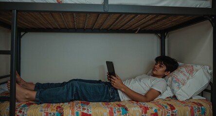 indian teenage boy on bunk bed using tablet relaxed
