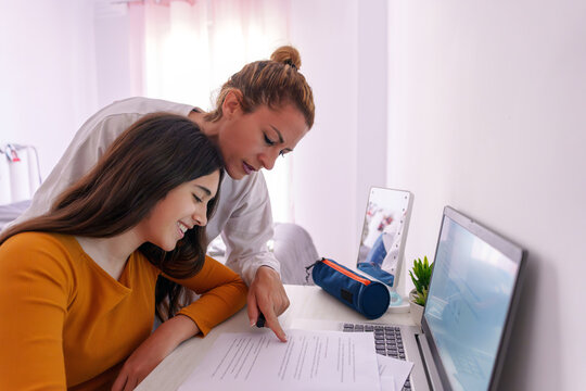Mother helping teenage daughter with homework using laptop at home