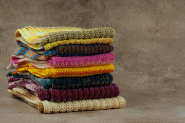 Many knitted scarves in a pile. Scarves for autumn and winter on a textured background.