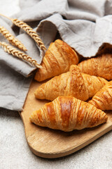Freshly baked croissants resting on wooden cutting board with wheat stalks