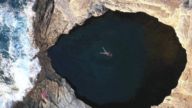  Stunning aerial top down slow motion view of a woman swimming in the Giola natural sea pool, lagoon. Thassos island, Greece