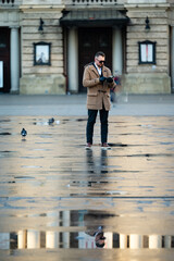 Urban solitude captured in a quiet square where reflections dance on rain-soaked pavement as a man...