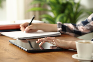 Student hands checking tablet and taking notes on notebook