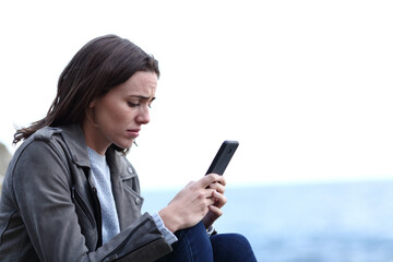Sad teen on the beach checking mobile phone
