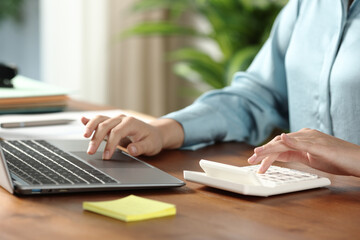 Office worker calculating with calculator and browsing on laptop