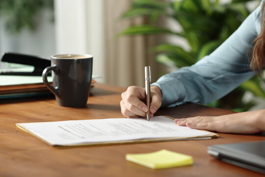 Office worker hands signing a paper contract on wooden table