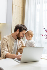 Bearded young caucasian man working from home while taking care of his little son