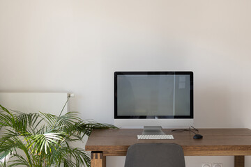 desktop computer with big empty screen, modern workplace interior with copyspace, white wall