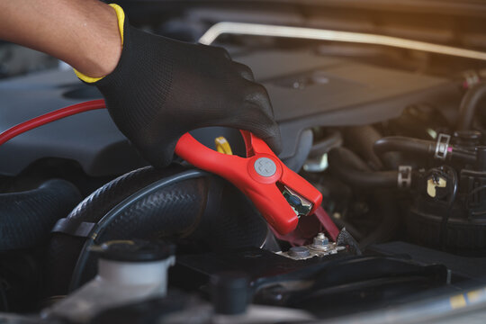 Fototapeta Hands in black gloves are carefully attaching red jumper cables to a car battery terminal, ready to jump-start a dead battery.