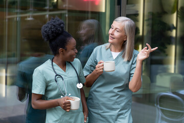 Two female doctors with cups with coffee in the elevator talking