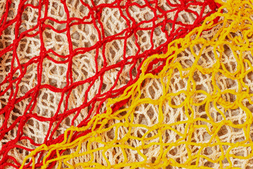 Colorful handmade mesh with red and yellow yarns over beige knit background. Vibrant net textures,...
