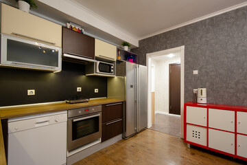 Apartment interior. Kitchen furniture. Kitchen set with dishwasher, oven and refrigerator. There is a humidifier on the red chest of drawers. Kitchen appliances. There is a corridor behind the passage