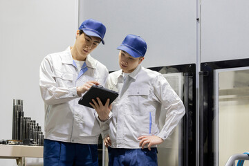 タブレットPCを持って機械を点検する作業員グループ