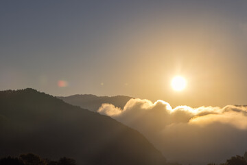 Golden morning sunlight bathes the misty mountain landscape, illuminating drifting clouds with a warm glow and creating a tranquil, ethereal atmosphere