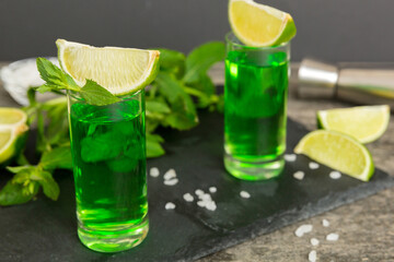 Sweet refreshing mint liqueur, with ice and mint leaves on table background, Shots with lime slice and mint flat lay