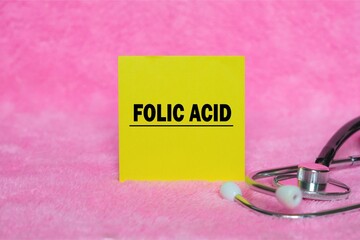 Folic Acid writing concept on sticky note isolated on pink background. stethoscope as decoration.