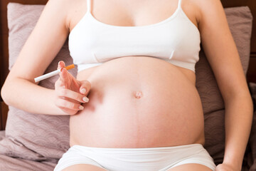 Pregnant woman smoking cigarette at home in bed