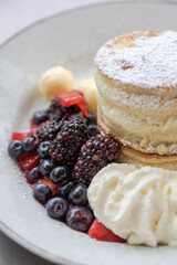 Close-up of fluffy Japanese souffle pancakes dusted with powdered sugar, served with fresh blackberries, blueberries, strawberries, vanilla ice cream, and whipped cream on white plate Delicious brunch