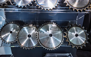 Close-up of shiny metal industrial sprockets or gears displayed on dark shelves, highlighting their...