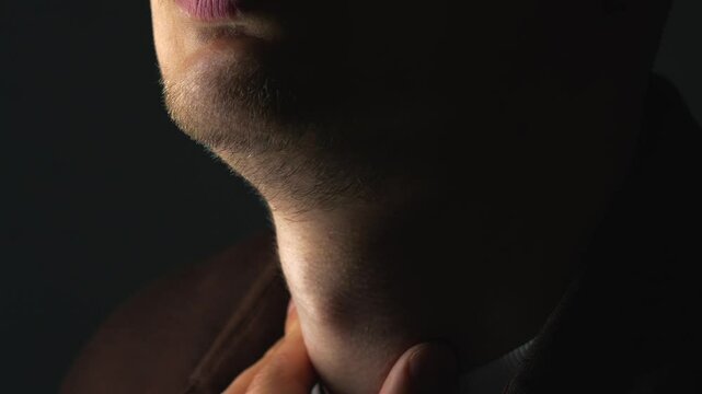 A man in a dark room swallows saliva.
Anatomy of the male body.
The Adam's apple moves when swallowing food.
Adam's apple on the neck