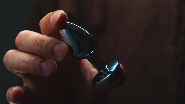 anal toy in hands close-up.
Metallic shiny anal plug.
Anal sex and pleasure.
Toys for adults.
Sex shop and metal dildo